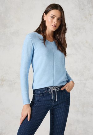Lichtblauw langemou top met een textuurafwerking, voorzien van een V-hals en een subtiele naad, gecombineerd met donker gestreepte denim broek en een gebonden patroon.