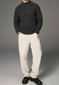 Dunkelgrauer Strickpullover mit hohem Kragen, kombiniert mit cremefarbenen, weit geschnittenen Hosen und schwarzen Schnürschuhen. Glatte Textur und lässige Passform.