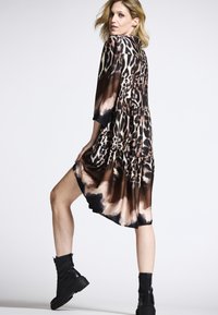 Leopardmuster-Kleid aus fließendem Stoff, mit Rundhalsausschnitt, Dreiviertelärmeln und einem gestuften Saum. Kombiniert mit schwarzen Kampfstiefeln.