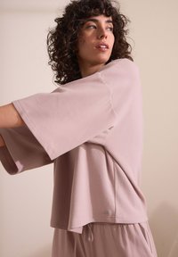 Maglietta rosa oversize a maniche corte in morbido tessuto con vestibilità rilassata, caratterizzata da un discreto dettaglio sull'orlo e un'etichetta in basso a sinistra.