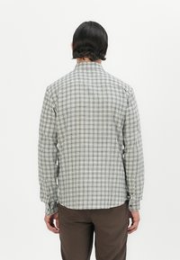 Camisa de manga larga con patrón de cuadros en gris y blanco, con un cuello clásico, puños abotonados y un corte relajado. Los botones tienen un tono dorado.