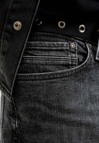 Tamnosive traperice s diskretnom teksturom, ukrašene metalnim detaljima i kontrastnim crvenim šavovima na džepovima i šavovima.