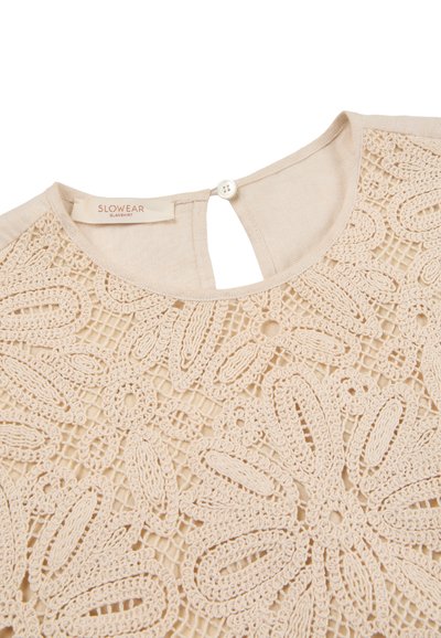 Beżowy top z koronki szydełkowej z misternymi wzorami kwiatowymi, okrągłym dekoltem, zapięciem na guziki z tyłu oraz metką z napisem "SLOWEAR OLANSHIRT".