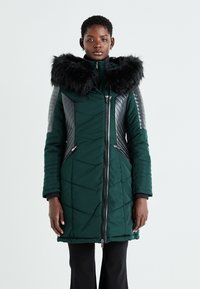 Zaļš šūnveida pūkains mētelis ar mākslīgo kažokādu uz kapuces, ādas akcenti uz pleciem, priekšējais rāvējslēdzējs un sānu kabatas. Strukturēts raksts sānos.