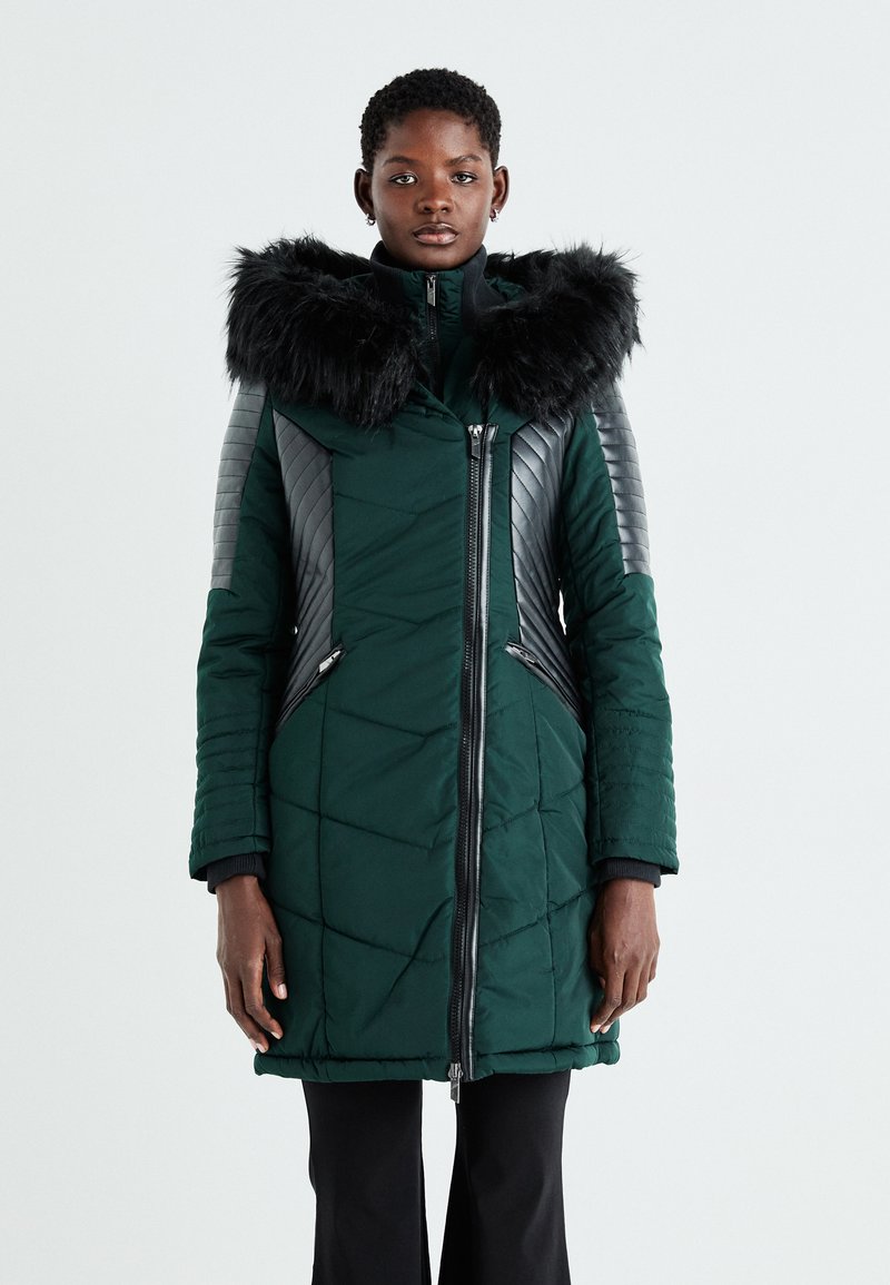 Zaļš šūnveida pūkains mētelis ar mākslīgo kažokādu uz kapuces, ādas akcenti uz pleciem, priekšējais rāvējslēdzējs un sānu kabatas. Strukturēts raksts sānos.