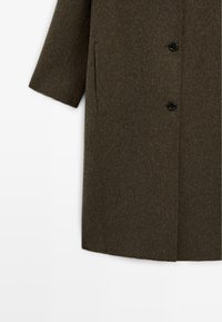 Cappotto in misto lana di un verde oliva scuro, con un taglio dritto, tasche laterali e due bottoni neri sul davanti.