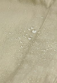 Gouttes d'eau perlant sur un tissu imperméable beige clair avec des coutures visibles.