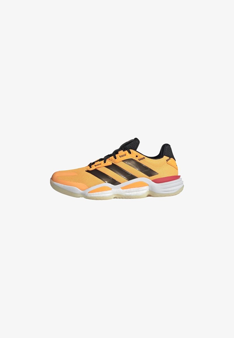 Chaussure de sport basse orange et noire avec des lacets noirs, une semelle blanche et un accent rouge près du talon, vue de profil.
