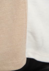 Twee aangrenzende stofstukken: één beige, de ander wit. Beide hebben een zachte textuur en een fijn breipatroon met zichtbare stiksels aan de randen.