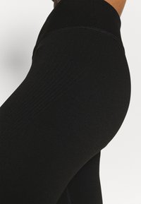 Schwarze nahtlose Leggings aus dehnbarem Material, mit einem hohen Bund und gerippter Textur an den Seiten für verbesserten Sitz und Komfort.