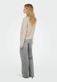 Suéter de punto beige con un corte relajado y mangas largas, combinado con unos jeans grises de pierna ancha y cintura alta. Tejido texturizado, detalles mínimos.