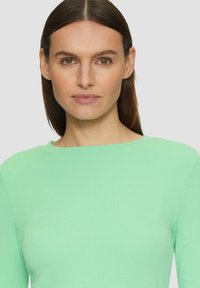 Un haut en maille côtelée vert clair avec un col bateau. La texture est lisse avec une coupe ajustée pour un look décontracté.