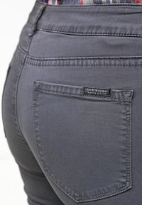 Los pantalones vaqueros de mezclilla gris cuentan con un bolsillo trasero con una etiqueta que dice "SCOTCH & SODA", detalles de costura sutiles y un ajuste entallado.