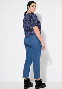 Top floreale blu a maniche corte abbinato a jeans blu a vita media con decorazioni in perle sui lati e stivali neri alla caviglia.