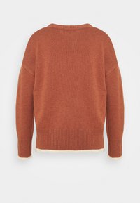 Pull en maille de couleur rouille avec un col rond, des épaules descendues et un ourlet à côtes. Présente un bord contrastant crème au bas.