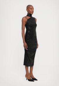 Black sequin dress with a fitted silhouette, halter neckline, and gathered texture. Worn with black pointed-toe heels.