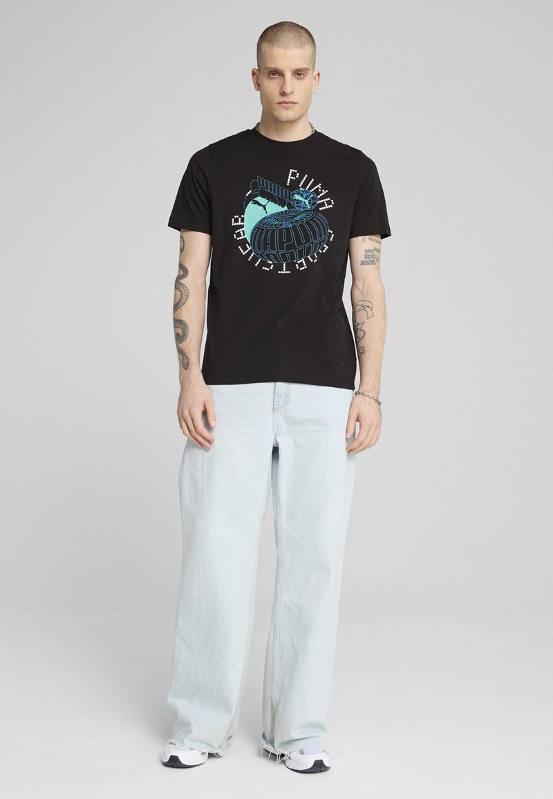 T-shirt nero a maniche corte con una stampa grafica colorata che presenta un design del globo. Indossato con jeans larghi blu chiaro e sneakers.