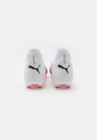 Scarpe da calcio bianche con parte superiore testurizzata, caratterizzate dal logo Puma nero e il testo "ULTRA", e tacchetti della suola di un rosso brillante per una migliore trazione.