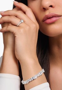 Gioielleria in cristallo trasparente caratterizzata da una pietra centrale ovale su un anello e un bracciale abbinato con pietre rettangolari e rotonde. Metallo di tonalità argento.