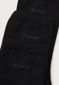 Juodi medvilniniai kojinės su raštuotų paviršių ir tamsiai pilku logotipu "BOSS". Suformuoti trys poros.