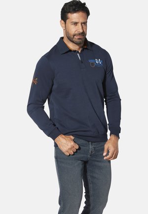 Navy long-sleeve polo shirt with a collar, featuring an embroidered logo and orange accents on the placket and sleeve. Paired with dark denim jeans.