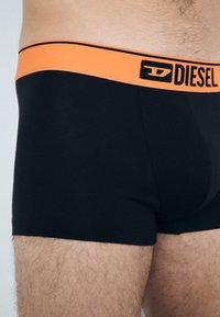 Boxer-briefs noirs avec une ceinture élastique orange portant le logo "Diesel". Le tissu semble lisse et ajusté.