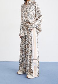 Skjorta i leopardmönster och vida byxor i beige och grått. Byxorna har vita ränder och en märkeslapp. Gjorda av ett mjukt, lätt material.