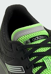 Čierna športová obuv s priedušným zeleným vrchným materiálom z siete, šedými akcentmi a čiernymi šnúrkami. Na boku je viditeľná nášivka s logom. Textúrovaný povrch.