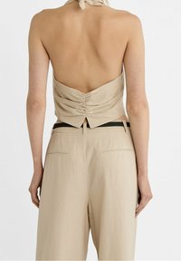 Beżowy top bez pleców z marszczeniami z tyłu, zestawiony z beżowymi spodniami z wysokim stanem, wyposażonymi w boczne kieszenie i czarny, pleciony pasek.