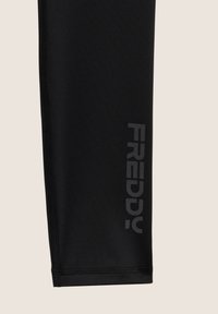 Leggings noirs en tissu extensible, avec un design épuré présentant un logo "FREDDY" gris bien visible le long de la couture latérale.