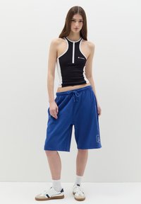 Black and white zip-up tank top paired with blue drawstring shorts; short design with a smooth texture and logo detail on the shorts.