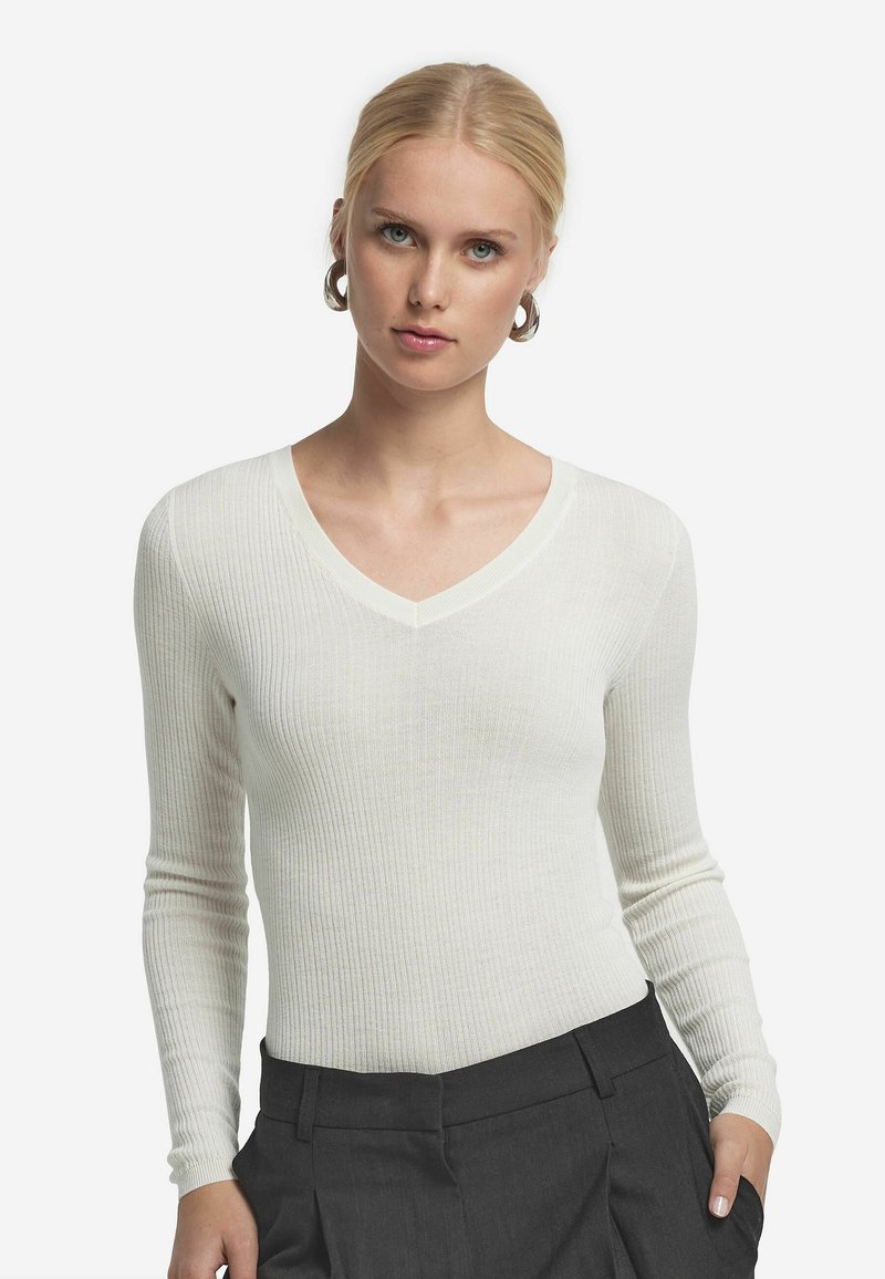 Vit ribbad långärmad topp med V-ringning. Har en figurnära passform och mjuk textur, ihop med högmidjade mörkgrå byxor.