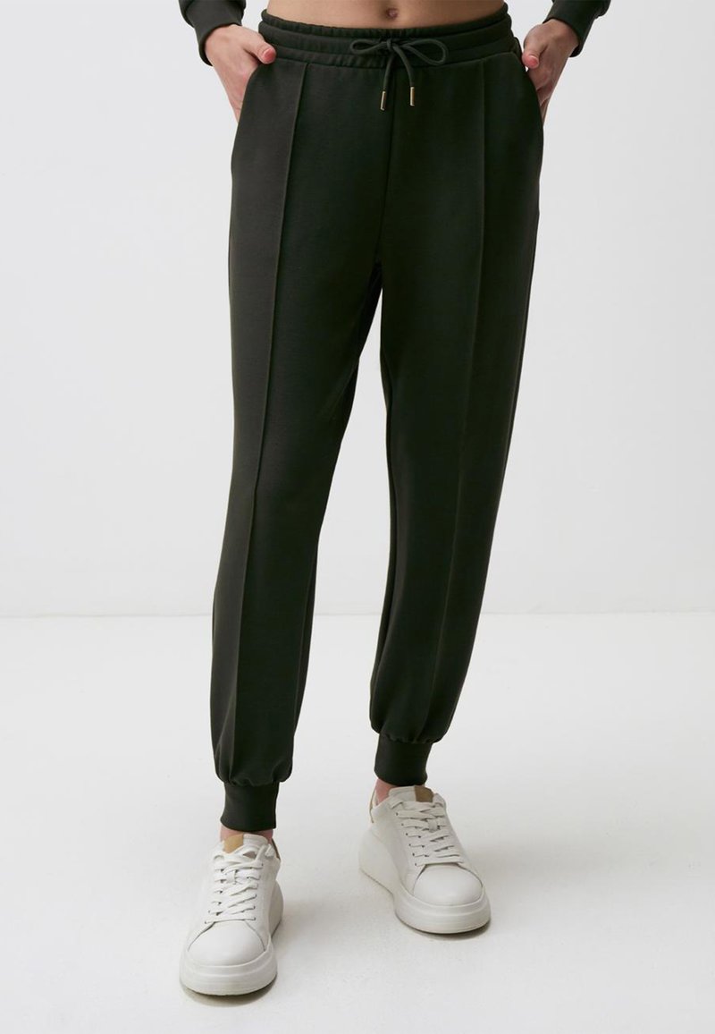 Dunkelgrüne Jogginghosen mit einem Kordelzugbund, schmal zulaufenden Säumen, Seitentaschen und weichem Stoff, kombiniert mit weißen Sneakers.