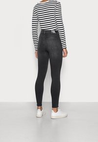 Pantalones ajustados de tiro alto negros con una textura suave, combinados con una camiseta de manga larga a rayas en blanco y negro y zapatillas blancas.