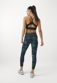 Reggiseno sportivo nero con un design a incrocio sulla schiena; abbinato a leggings aderenti con un motivo botanico colorato in verde e blu.