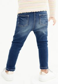 Modré džíny z denimu s úzkým střihem, zadními kapsami a mírným vyblednutím. V kombinaci s bílými teniskami s kovovým akcentem.