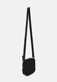 Svart crossbody-veske med rektangulær form, laget av stoff, med glidelåslukking og justerbar stropp for enkelhet.