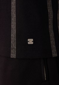 Sort sweatshirt med et struktureret stribemønster i grå, med et lille sølvlogo fastgjort nær sømmen og en lynlås i siden.