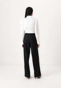 Blouse blanche ajustée avec un col montant, associée à un pantalon noir à jambe large. La blouse présente des coutures détaillées et des manches à poignet.