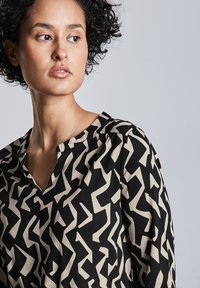 Blusa a maniche lunghe nera con un motivo astratto crema, caratterizzata da scollatura a V e tessuto morbido e strutturato per una vestibilità rilassata.