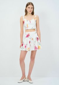 Florales Zweiteiler-Set mit einem weißen Crop-Top mit verstellbaren Trägern und einem passenden, weit ausfallenden Rock, beide mit bunten Blumenmustern verziert.