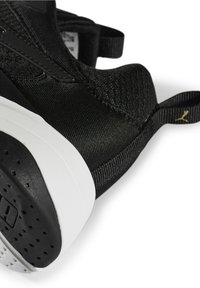 Talons de baskets noirs avec une semelle intermédiaire blanche et une semelle extérieure noire, présentant un tissu en maille texturée et un logo Puma doré sur la languette de tirage.