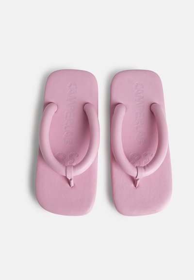 Lyserøde gummiflip-flops med en tyk, rund rem og struktureret sål. Mærkenavnet er indprentet på sålen.