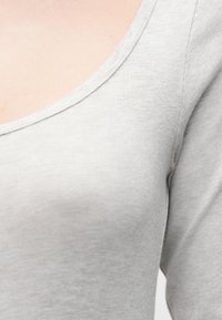 Ανοιχτό γκρι εφαρμοστό τοπ με λαιμόκοψη scoop, κατασκευασμένο από ύφασμα με ριμπ υφή. Ορατές ραφές κατά μήκος της ραφής του ώμου.