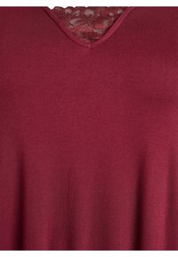 Vijoličasti top z V-izrezom in vložkom iz čipke na izrezu, izdelan iz gladkega blaga. Tekstura je mehka in rahlo prožna.