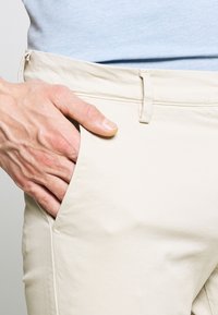 Beige, slim-fit stoffen gemaakt van katoen, met een zijzak en een platte voorkant, met een gladde textuur en minimale stikseldetails.
