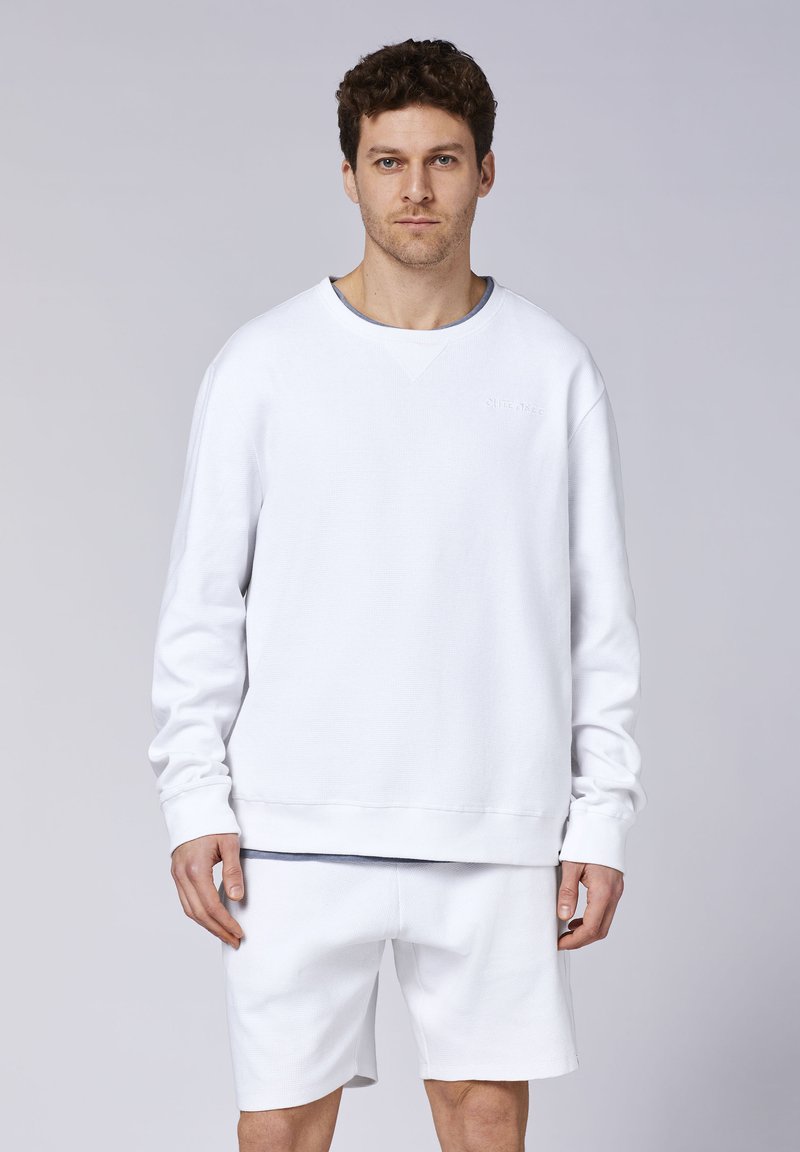 Weißes Sweatshirt mit strukturiertem Gewebe und gerippten Bündchen, kombiniert mit passenden weißen Shorts. Verfügt über ein kleines Logo auf der Brust.