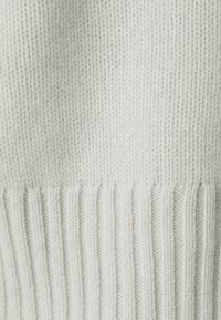 Tissu de pull tricoté gris clair avec une texture côtelée à l'ourlet, présentant des points serrés et bien espacés partout.