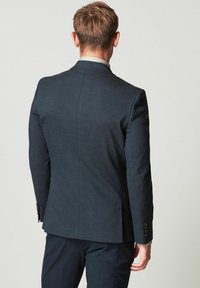 Granatowa marynarka o dopasowanym kroju, gładkiej fakturze i zapięciach na guziki. Projekt zawiera pojedynczy rozcięcie z tyłu.