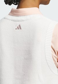 Hvid strikket ærmeløs vest med et tekstureret mønster, der har en lys pink krave og et diskret brunt Adidas-logo på bagsiden.